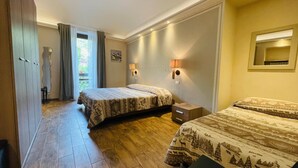 Quarto de hotel com duas camas, piso de madeira, uma mesinha e uma janela com cortinas.