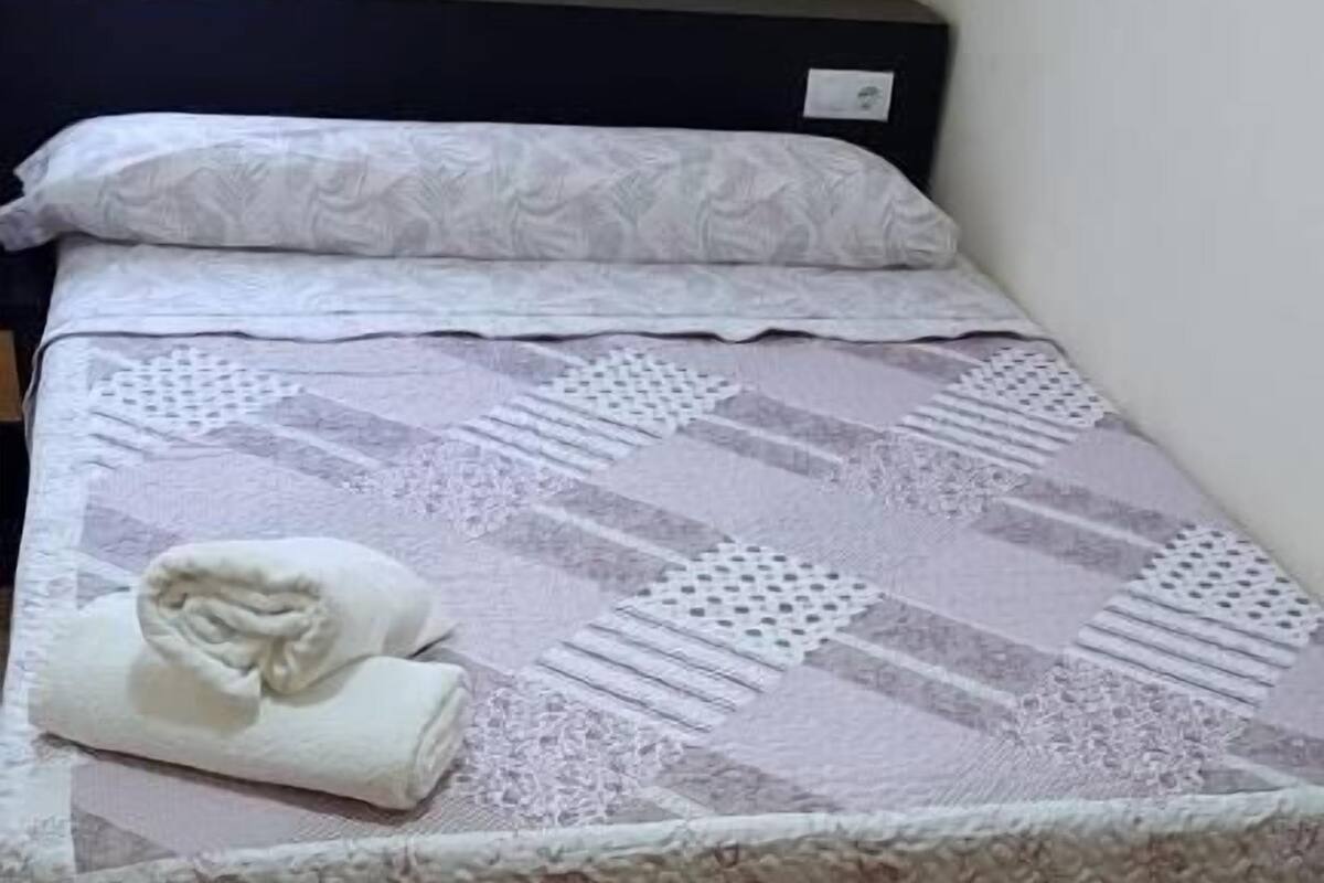 A neatly made bed with a patterned bedspread and a folded towel on the left side.