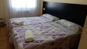 A double bed with a patterned bedspread, two pillows, and a rolled towel on the bed. - Noja Rooms (O Pino)