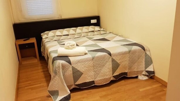 A small, neatly arranged bedroom with a bed, a bedside table, and a window. - Noja Rooms (O Pino)