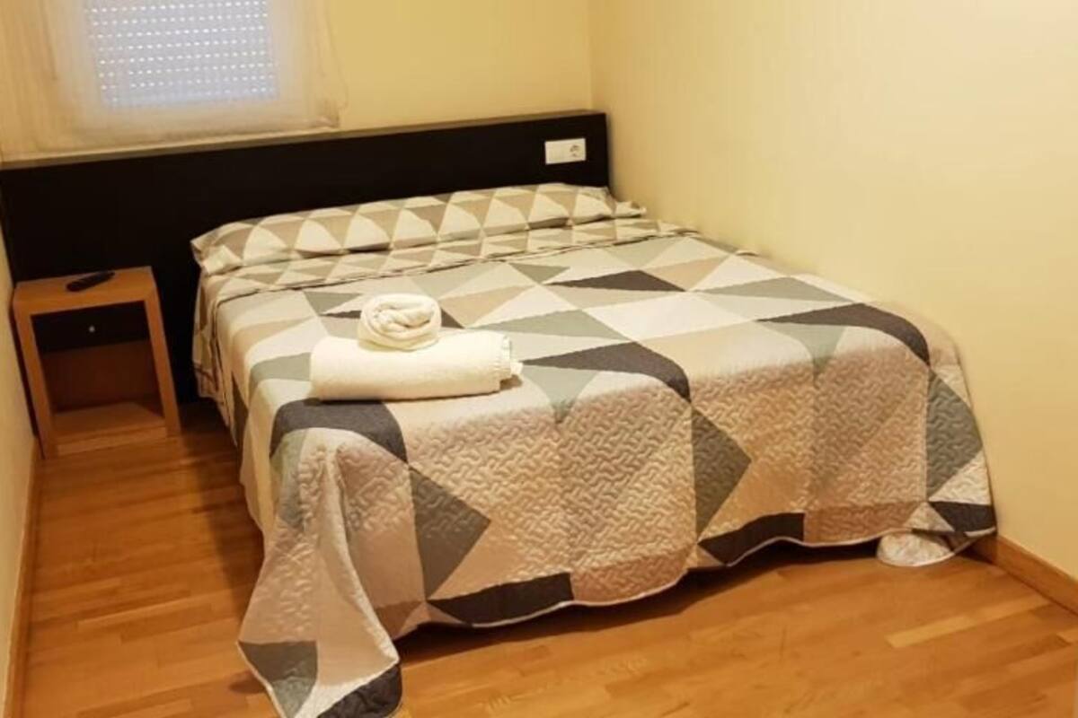 A small, neatly arranged bedroom with a bed, a bedside table, and a window.