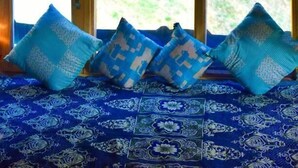Una habitación con alfombra azul estampada, techo de madera y ventana con vista a follaje.