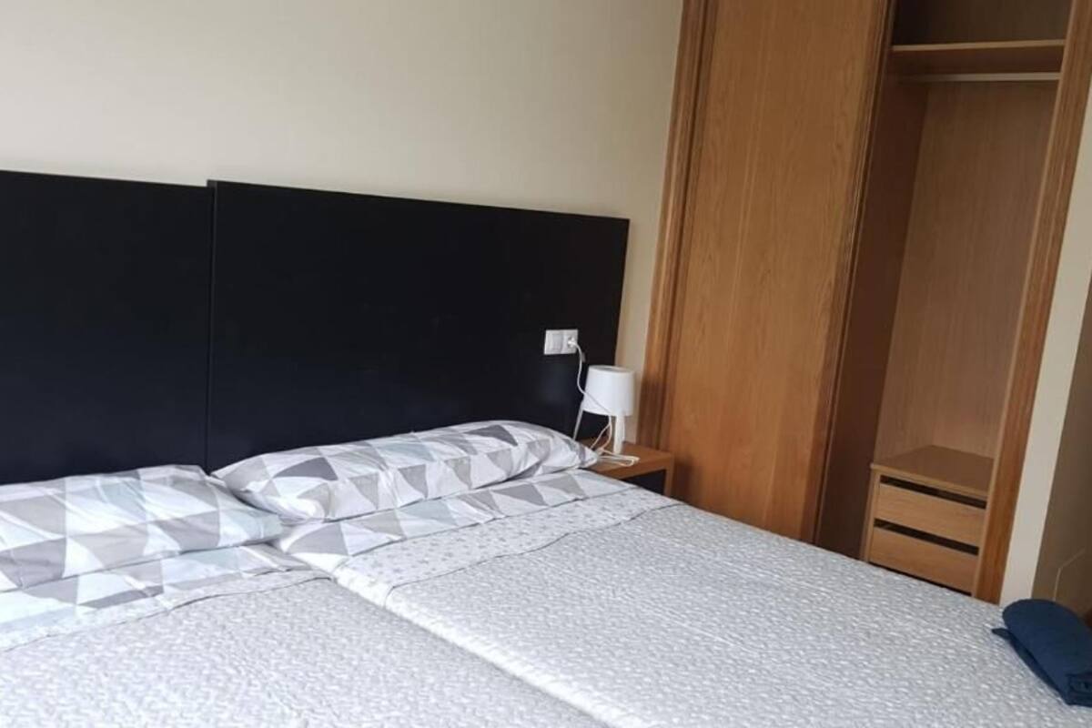 A neatly made bed with a patterned bedspread and pillows, a bedside table with a lamp, and a wooden wardrobe.