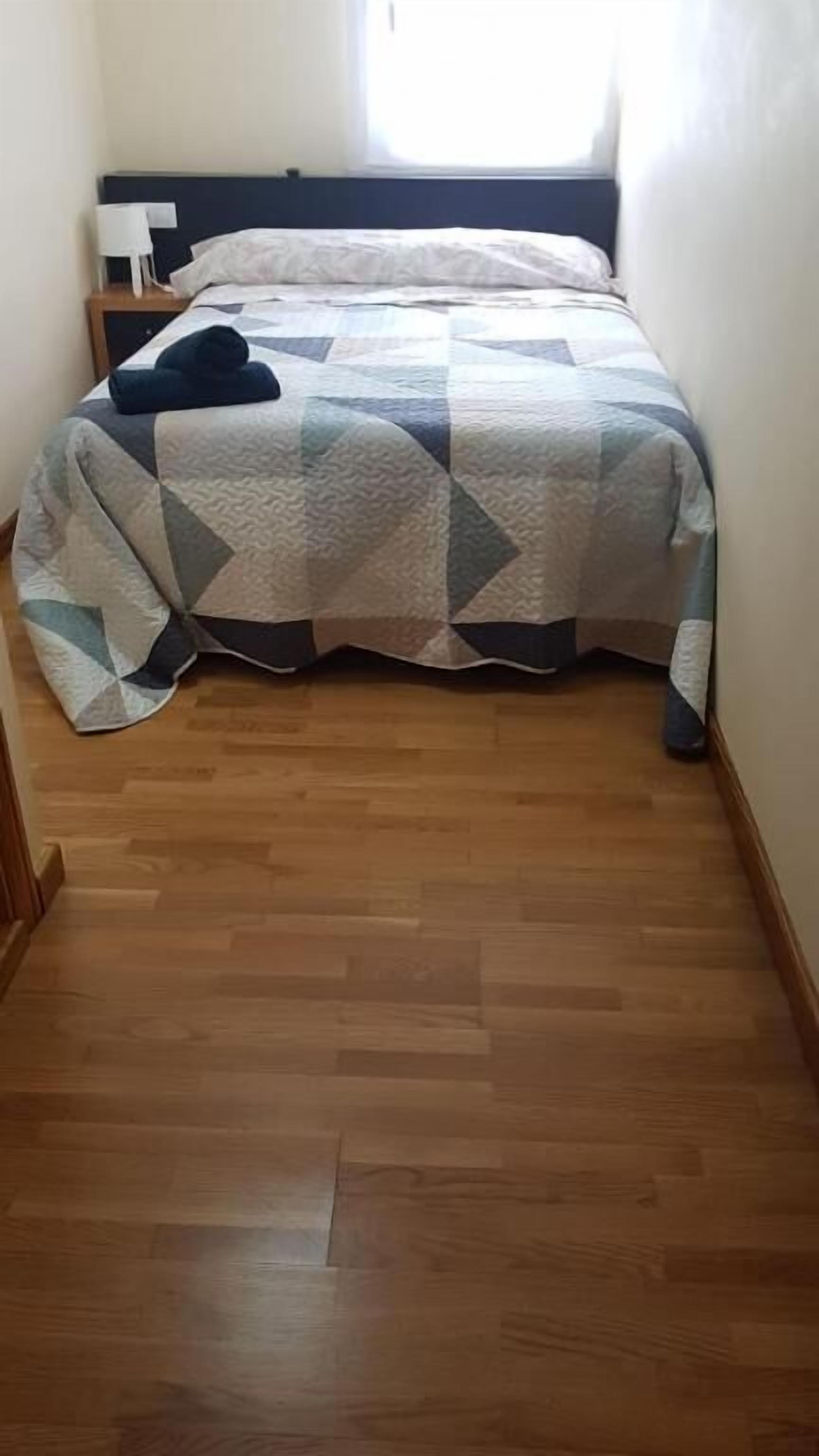 Ein schmaler Flur, der zu einem Bett mit einem geometrischen Muster auf der Tagesdecke führt.