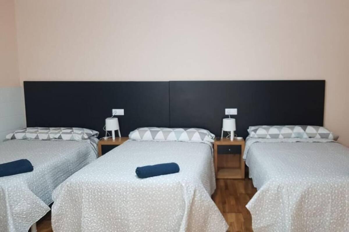 A hotel room with two single beds, each with a pillow and a small bedside table with a lamp.