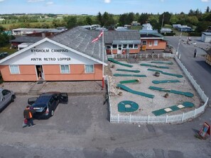 Un bâtiment du camping Bygholm, orné d’une enseigne rétro représentant des puces, une aire de stationnement avec des voitures et un petit drapeau.