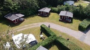 A campsite with three red cabins, a gravel path, and a neatly trimmed hedge. - Bygholm Camping Thy (Vesløs)