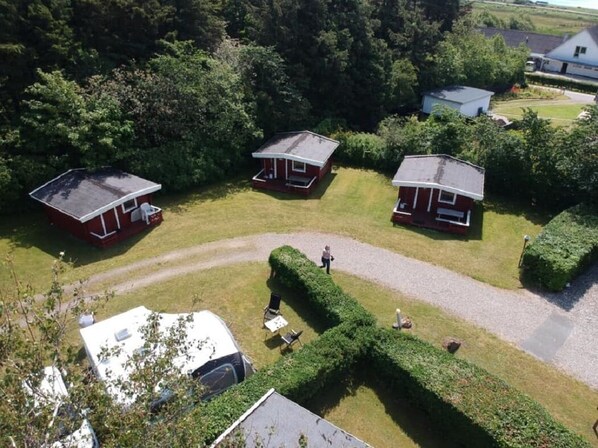 Un terrain de camping avec trois cabanes rouges, un chemin de gravier et une haie soigneusement taillée.