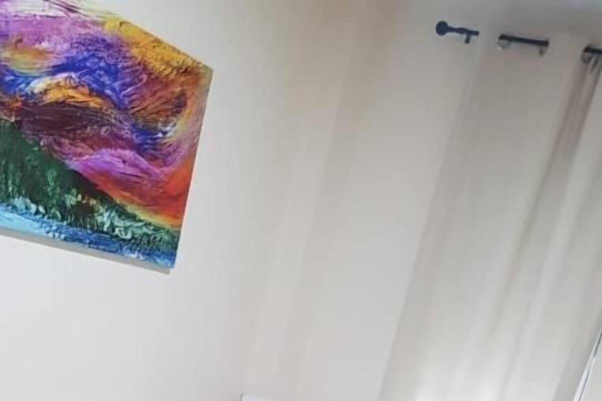 Une chambre à coucher avec un lit, une chaise, un tableau au mur et une fenêtre avec des rideaux.