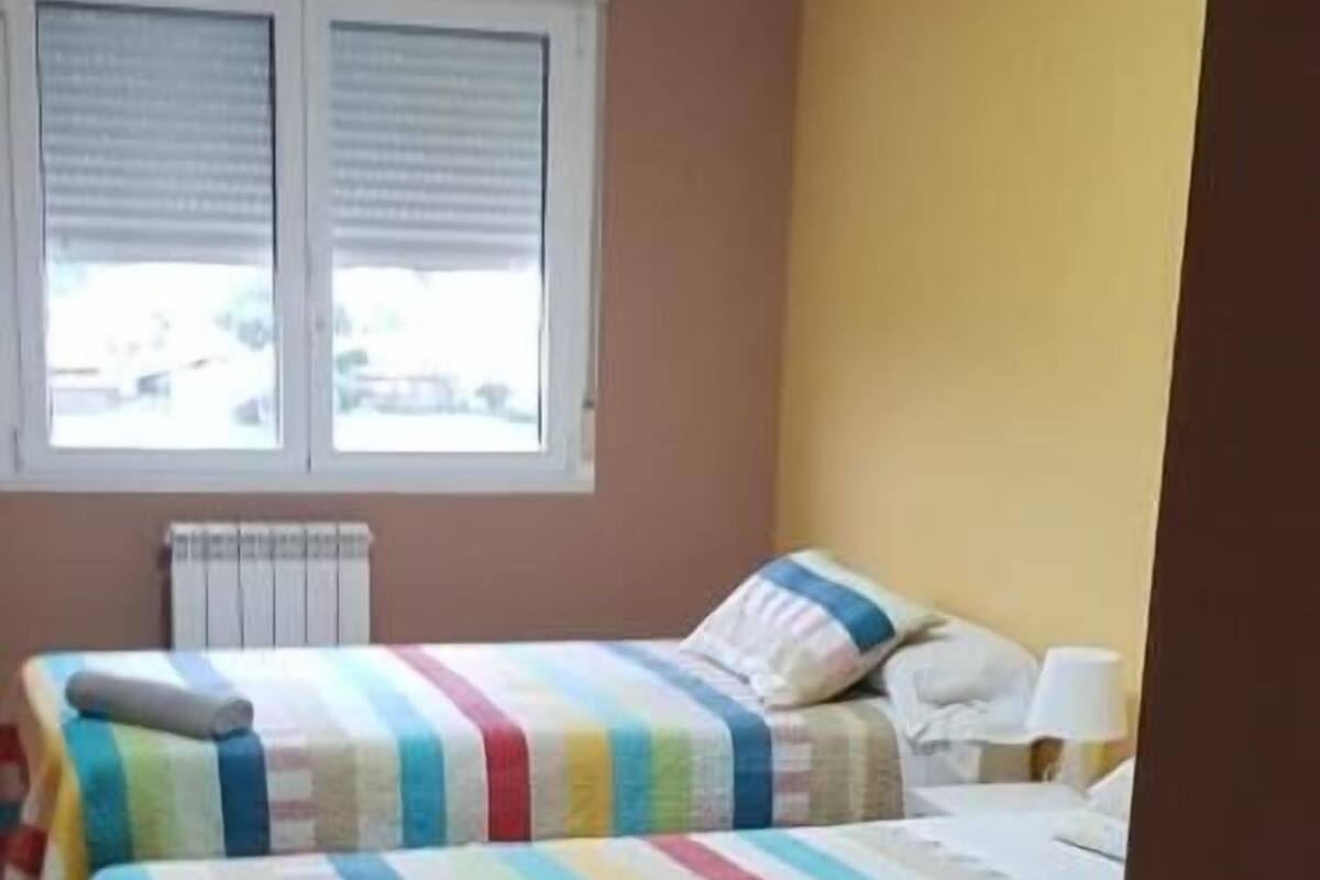 Une chambre avec deux lits, chacun doté de draps à rayures, une fenêtre avec des stores et un radiateur.