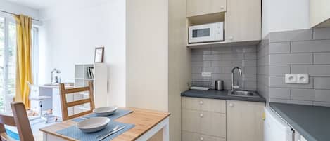 Cocina compacta con microondas, lavamanos y armarios. Hay un comedor con mesa y sillas.
