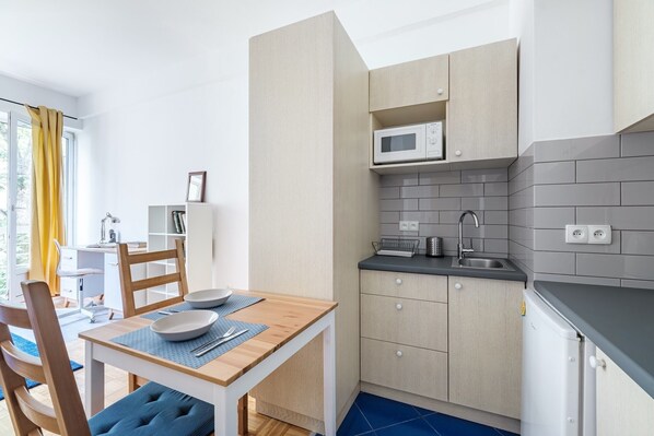 A compact kitchen with a microwave, sink, and cabinets. There is a dining area with a table and chairs.