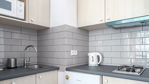 A kitchen with grey tiles, a stainless steel sink, a kettle, a small fridge, and wooden cabinets. - Friends Avenue Apartment (Warsaw)