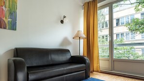 A room with a black leather sofa, a blue rug, a floor lamp, and a large window with curtains. - Friends Avenue Apartment (Warsaw)
