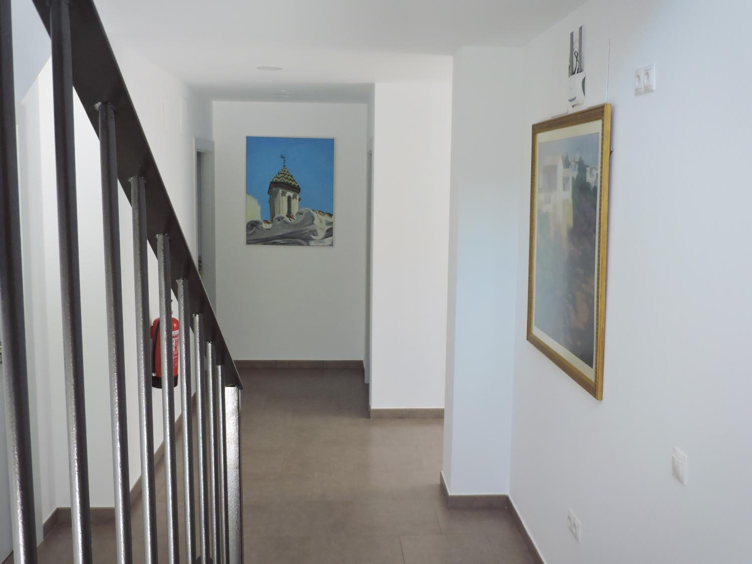 A hallway with a staircase, a painting on the wall, and a framed picture.