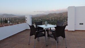 A terrace with a table and chairs, a lantern, and a view of mountains. - Hostal Delia (Álora)