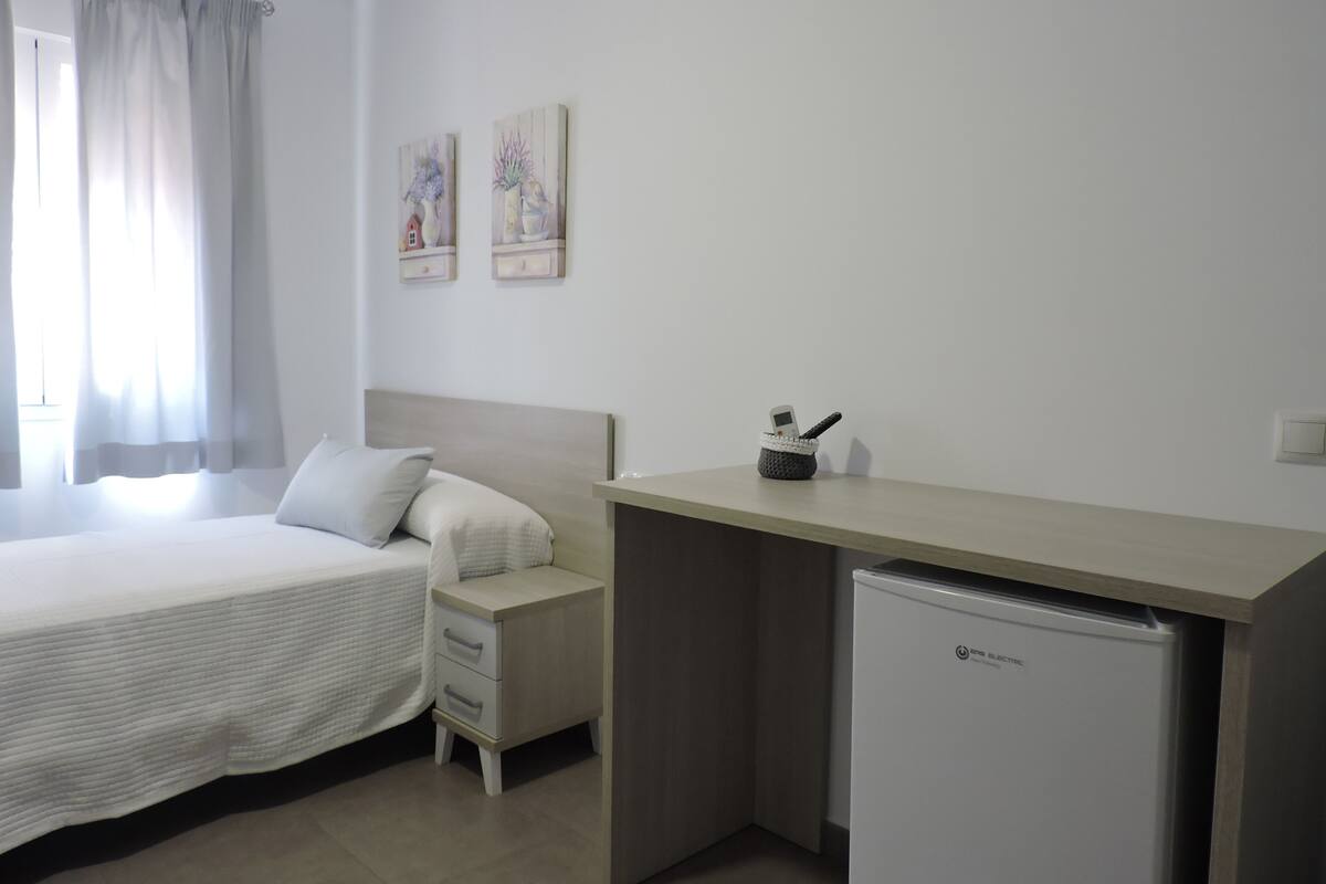A hotel room with a bed, a desk, a small refrigerator, and two paintings on the wall.