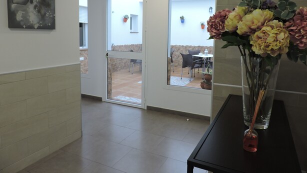 A reception area with a glass door leading to a patio, a vase with flowers on a table, and a painting on the wall. - Hostal Delia (Álora)