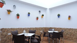 An outdoor patio with stone walls, tiled flooring, and tables with chairs. - Hostal Delia (Álora)