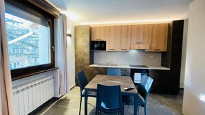 A modern kitchen with wooden cabinets, a dining table with chairs, and a window overlooking a cityscape. - VILLA LINDA - Studio  sleeps 2-3 (Bardonecchia)