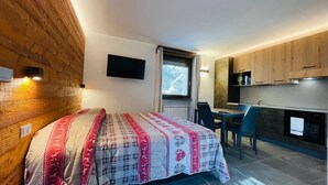 A compact room with a bed, a small desk, a television, and a kitchenette. - VILLA LINDA - Studio  sleeps 2-3 (Bardonecchia)