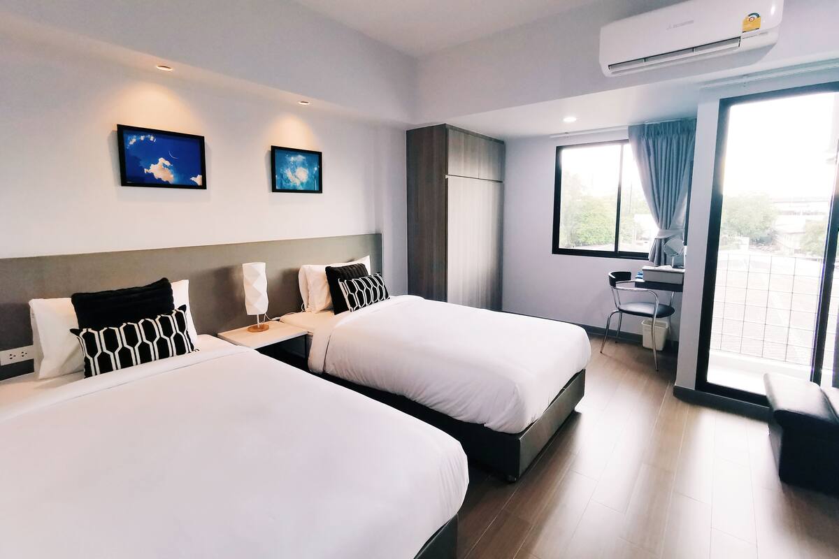 A hotel room with two beds, a desk, a chair, and a large window with curtains.