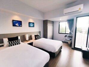 Ett hotellrum med två sängar, ett skrivbord, en stol och ett stort fönster med gardiner.