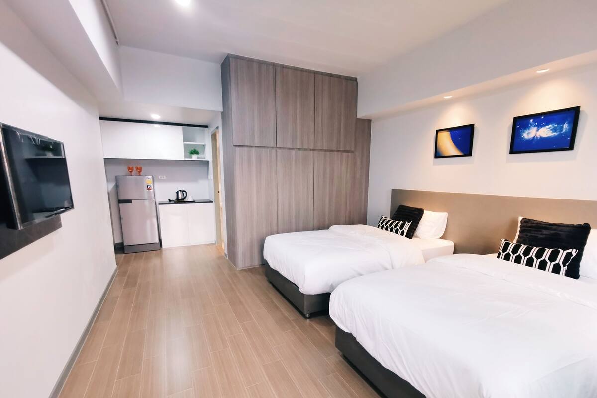 A hotel room with two beds, a kitchenette, and a TV mounted on the wall.