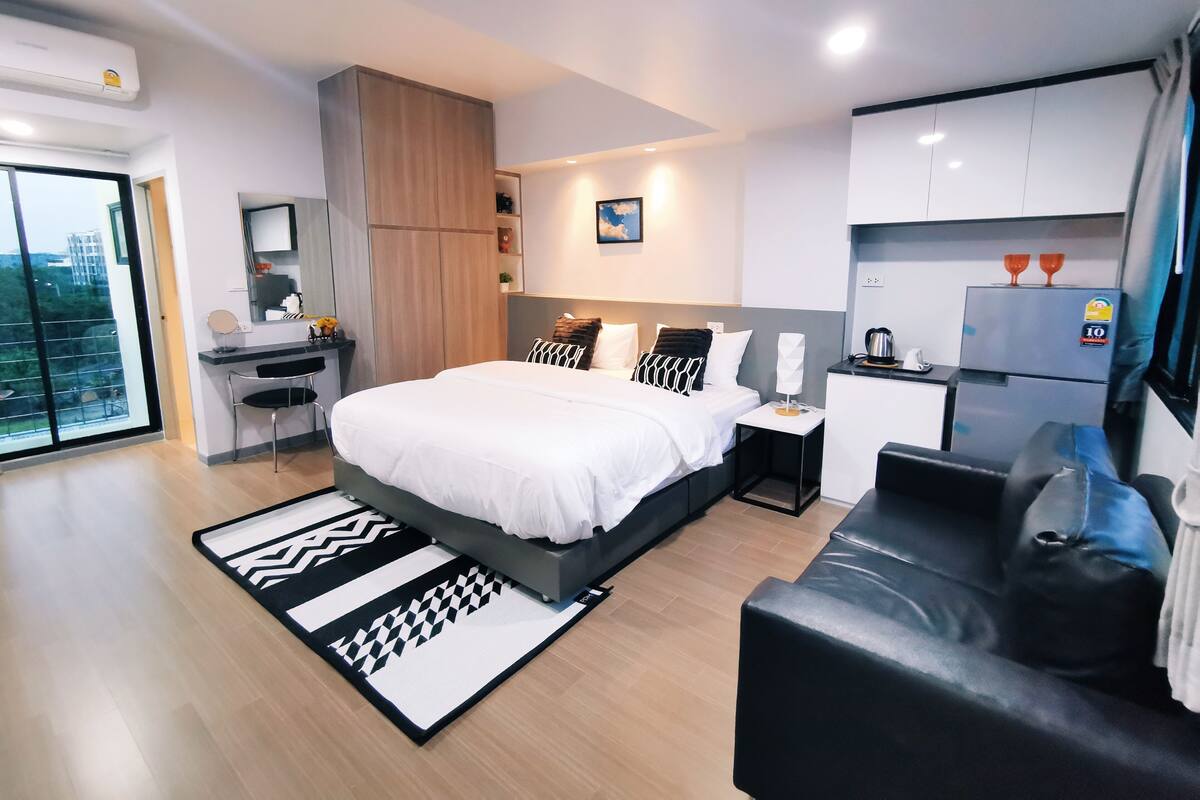 A modern bedroom with a large bed, a desk, and a kitchenette.