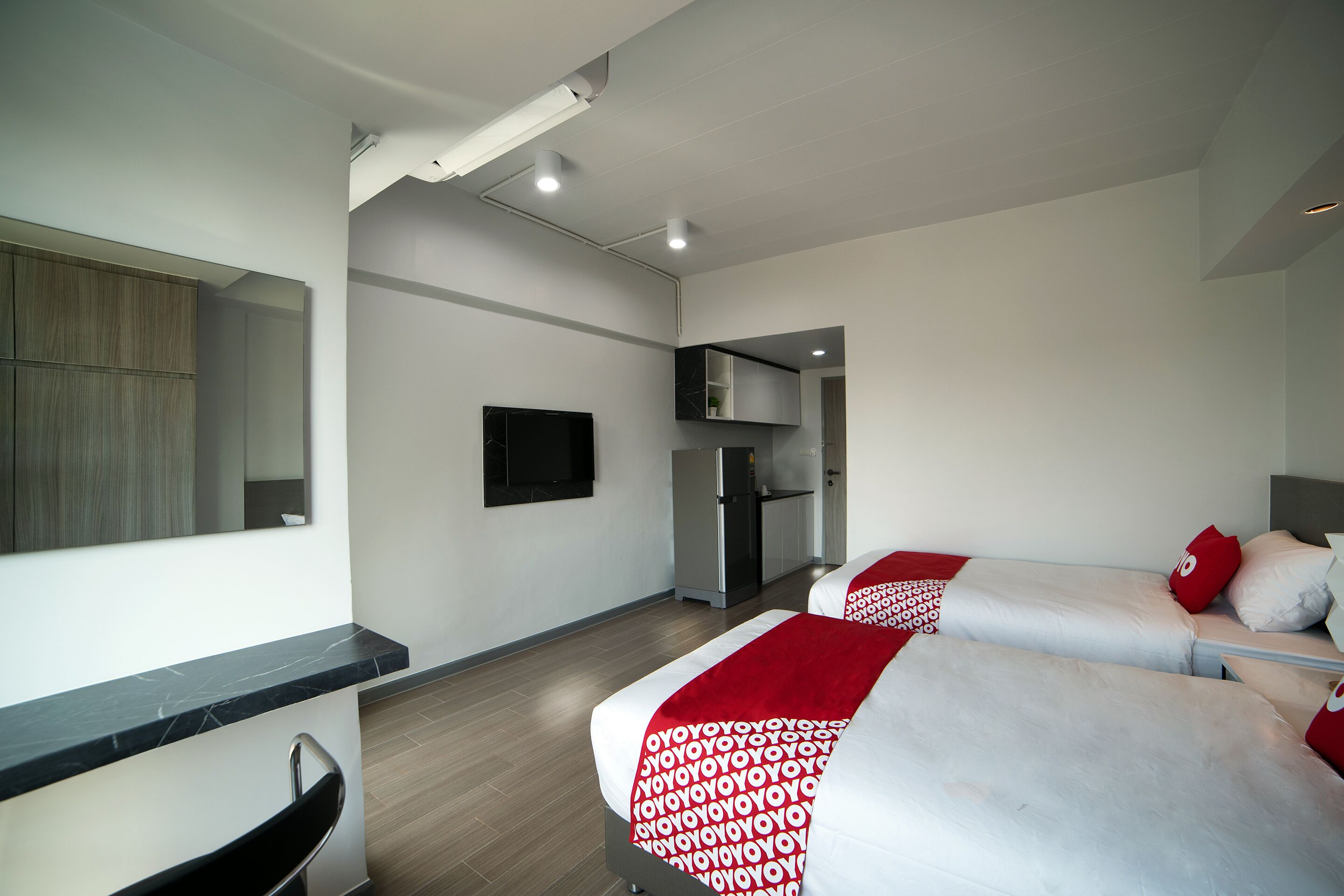 Habitación de hotel moderna con televisión de pantalla plana, kitchenette y dos camas con ropa de cama roja y blanca.