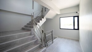 A staircase with metal railings and grey tiles, leading to a room with a large window and a ceiling light. - Star Sukhumvit (Bangkok)