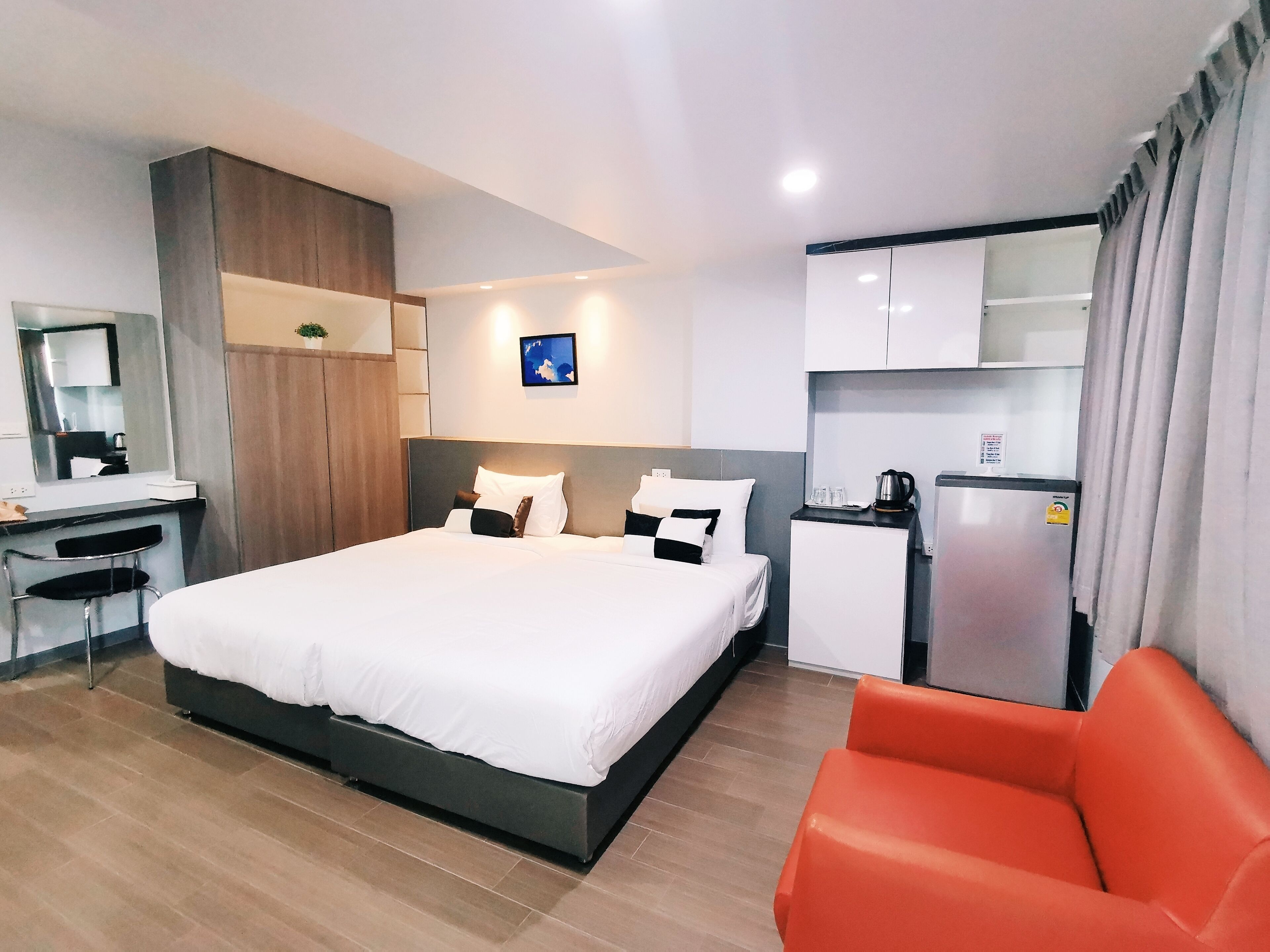 A modern hotel room with a large bed, a desk, a chair, a small kitchenette, and a bathroom.