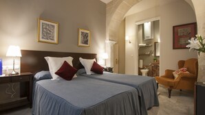 Ein Hotelzimmer mit zwei Betten, einem Nachttisch, einem Sessel und einem durch einen Bogen erreichbaren Badezimmer.