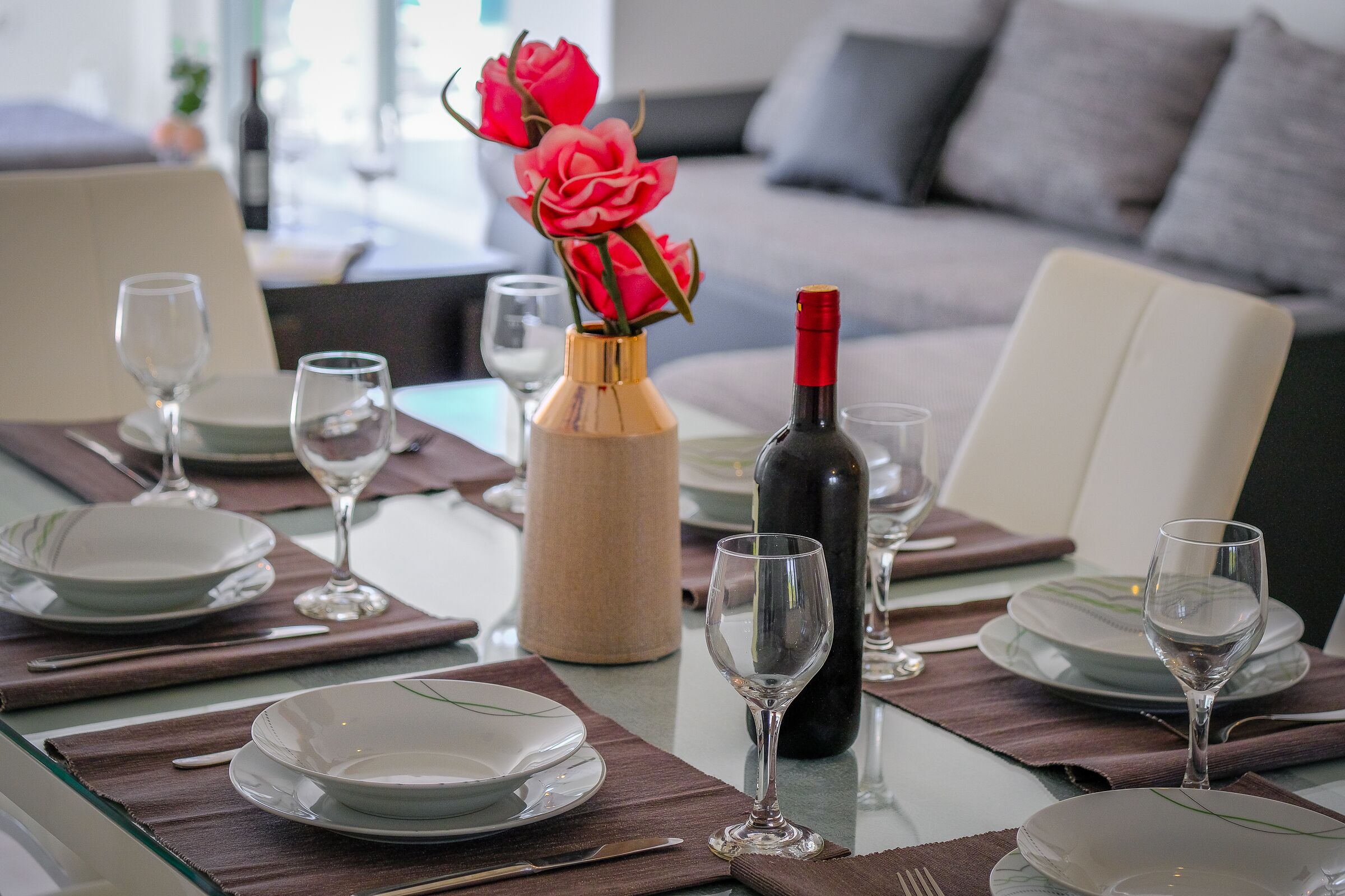 A dining table set with plates, glasses, and a bottle of wine, with a vase of flowers in the center.