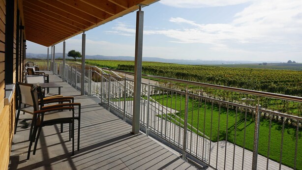 A covered outdoor area with a wooden deck, metal railing, and several chairs. - Apartment 3 terrace location Berg - Weingut Schaaf (Nordheim)