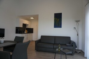A modern living room with a sofa, a dining table, and a kitchen in the background.