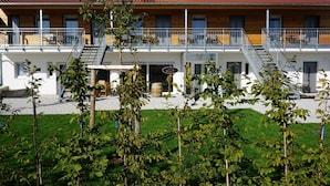 Un bâtiment à deux étages, doté d’un toit recouvert de tuiles rouges, de balcons avec des garde-corps en métal et d’un espace d’entrée pavé agrémenté d’une jardinière en forme de tonneau.