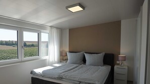 Une chambre avec un grand lit, deux tables de chevet avec des lampes, une fenêtre avec des rideaux et une vue sur un champ.