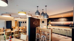 L’intérieur d’un restaurant est aménagé avec des tables et des chaises en bois, des luminaires suspendus et un coin bar doté de tabourets.