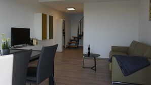 Uma sala de estar moderna com um sofá, uma mesa de jantar com cadeiras, uma televisão e uma escada que leva a outro andar.
