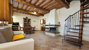 A spacious living area with a fireplace, wooden ceiling beams, a dining table, and a staircase. - La Fonte di Montebuono (Magione)