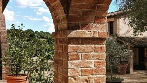 A brick archway with potted plants, a courtyard, and a building with a tiled roof. - La Fonte di Montebuono (Magione)