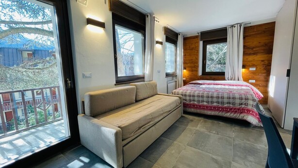 A bedroom with a bed, a sofa, and a large window. - Villa Linda - STUDIO sleeps 4 (Bardonecchia)