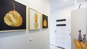 A hallway with three framed botanical prints on the wall, a white door, and a small wooden table with two ceramic animal figures. - Friendy Apartment    (Kraków)