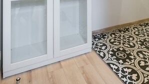 A white cabinet with glass doors, a wooden shelf with decorative items, and patterned floor tiles. - Friendy Apartment    (Kraków)