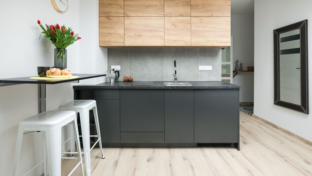 A modern kitchen with a central island, dark grey cabinets, wooden upper cabinets, a black countertop, and a white bar stool. - Friendy Apartment    (Kraków)
