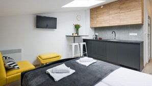 A modern hotel room with a bed, a small kitchen area, a yellow chair, and a TV mounted on the wall. - Friendy Apartment    (Kraków)