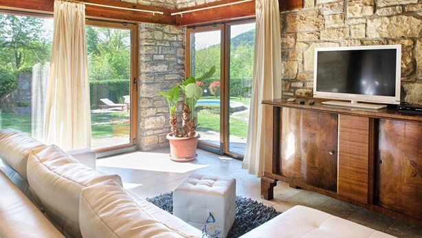 A spacious living room with a stone wall, a large window, a sofa, a television, and a potted plant. - Charming 2BR Villa with pool for 4+1, for small groups, pet-friendly (Buzet)