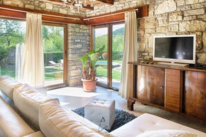 A spacious living room with a stone wall, a large window, a sofa, a television, and a potted plant. - Charming 2BR Villa with pool for 4+1, for small groups, pet-friendly (Buzet)