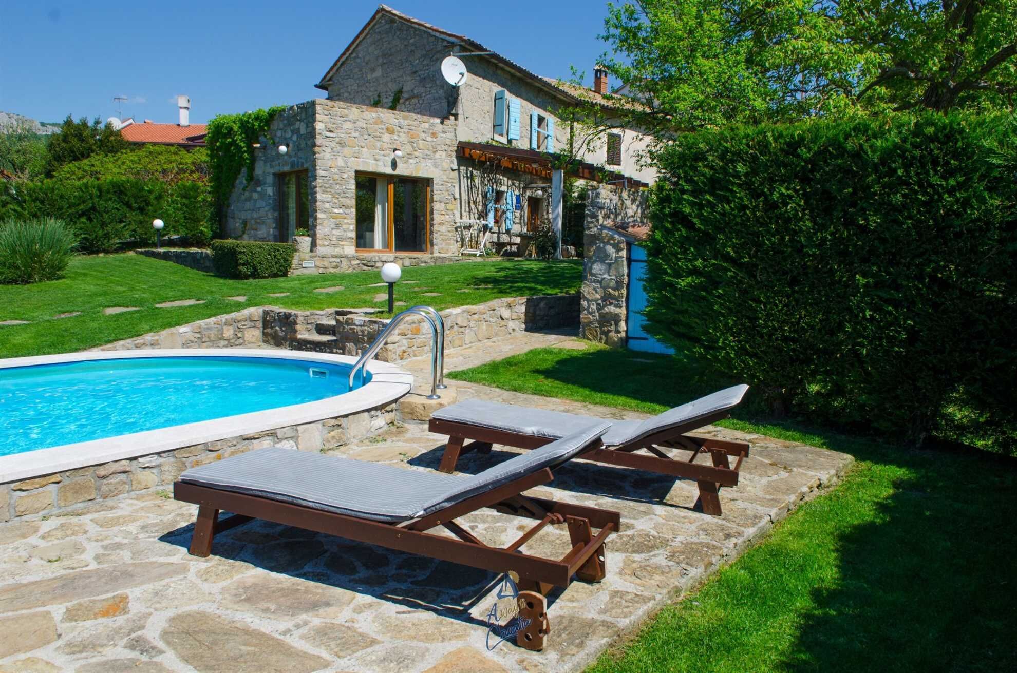 Una casa in pietra con piscina, due poltrone da relax e un prato curato.